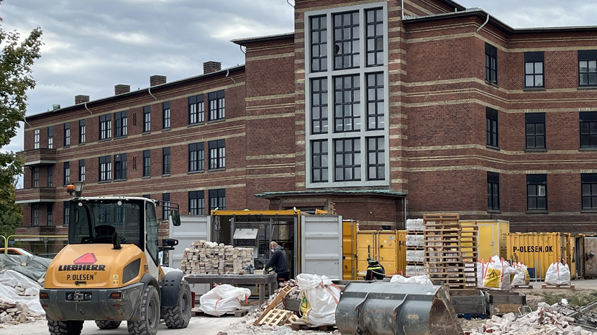 Brick building on a construction site. Bricks are beeing picked down and cleaned for new use. Construction cars in front. Picture