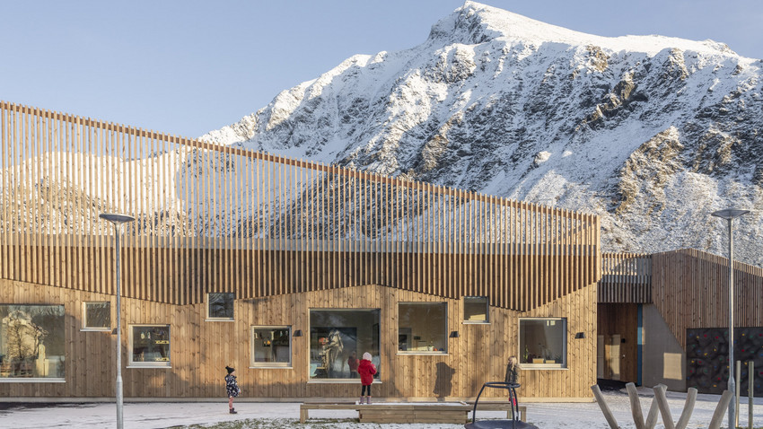 Skolefasade med spiler på taket og massivtre. Fjellandskap. Foto