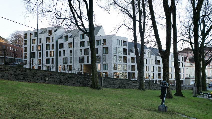 Boligfasade i grå murstein bakenfor en grønn park. Illustrasjon