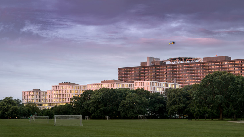 Helikopter flyver over Rigshospitalet. Park med fodboldbane foran. Foto