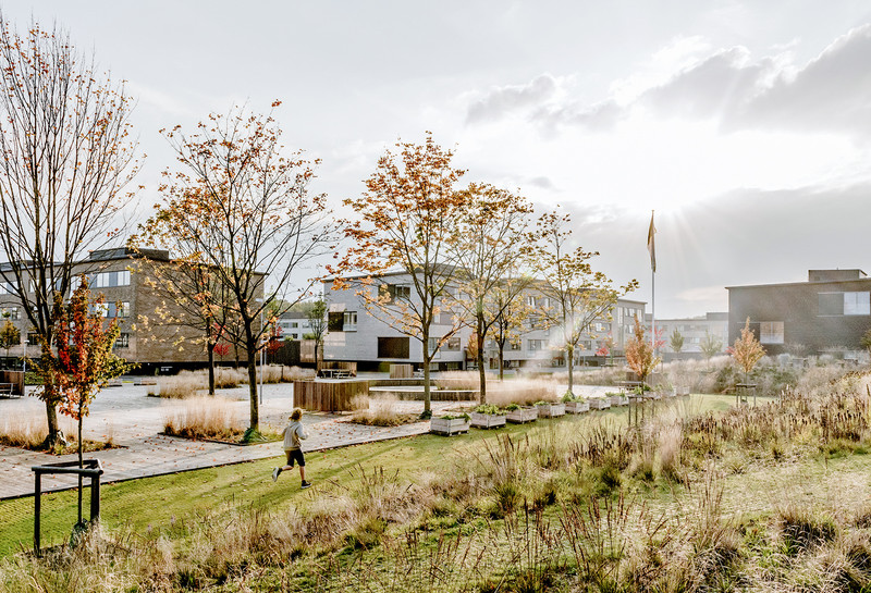 Børn løber på græsplænen foran tre boligblokke. Foto