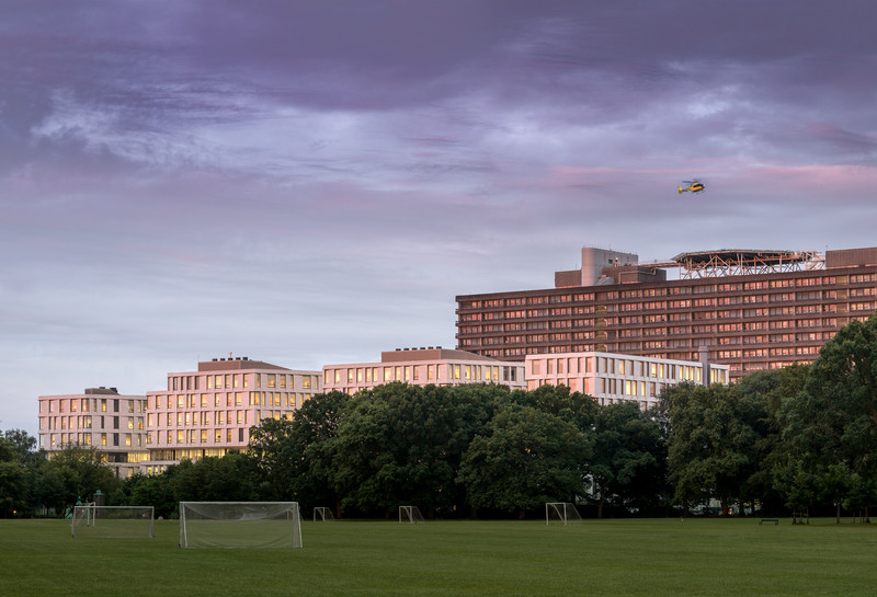 Helikopter flyver over Rigshospitalet. Park med fodboldbane foran. Foto