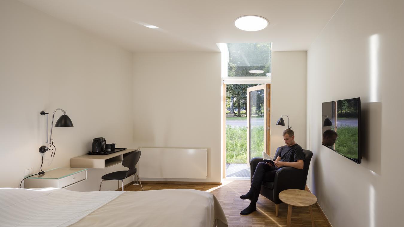 Man sitting in armchair reading in patient room, with open balcony door. Photo