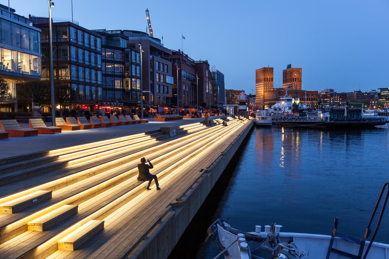 Opplyst brygge med Oslo Rådhus i bakgrunnen. Foto.