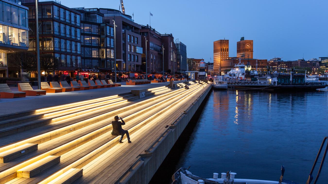 Opplyst brygge med Oslo Rådhus i bakgrunnen. Foto.