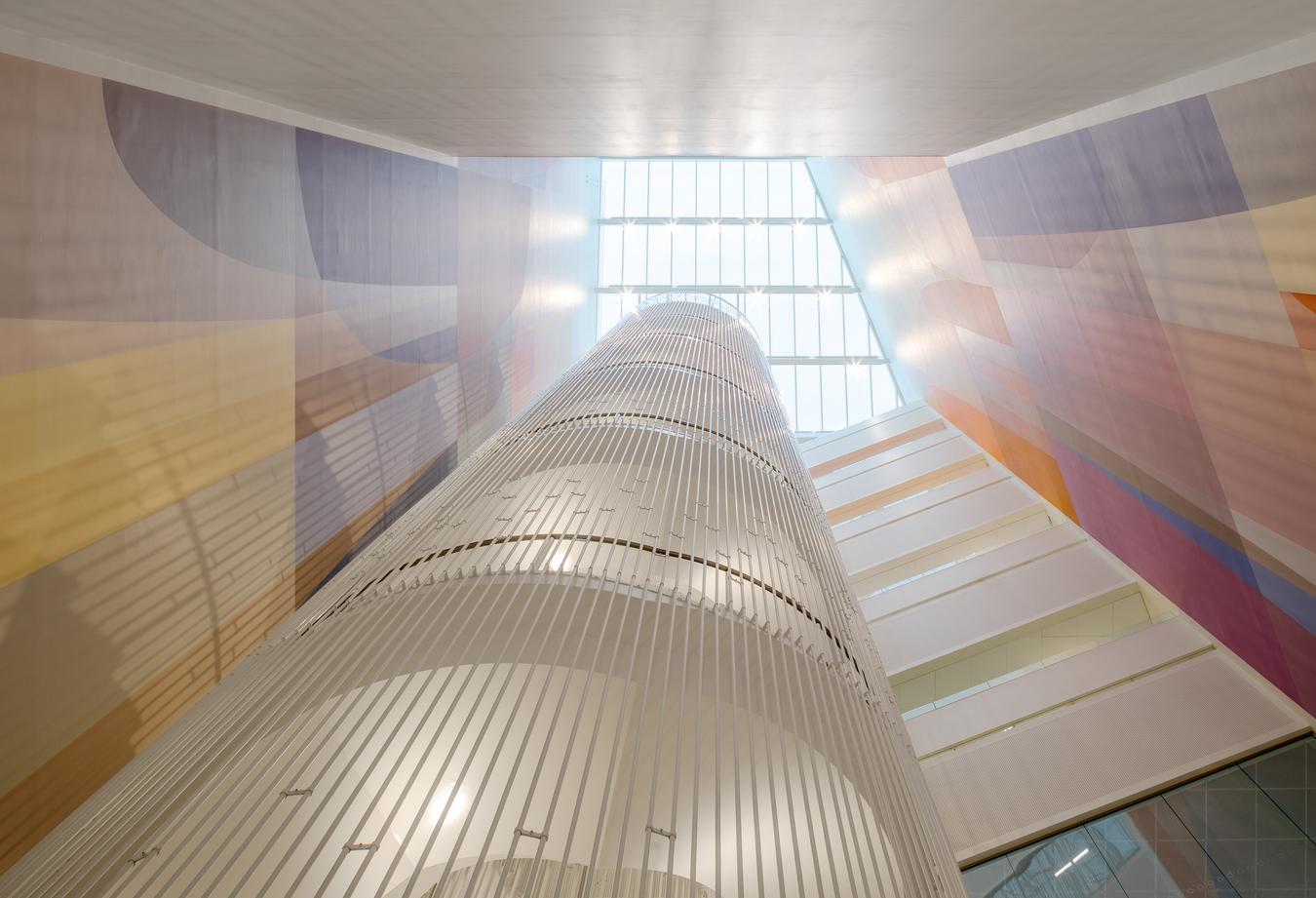 Large white spiral staircase with glass roof at the top. Abstract art follow the stairs all the way up. Photo