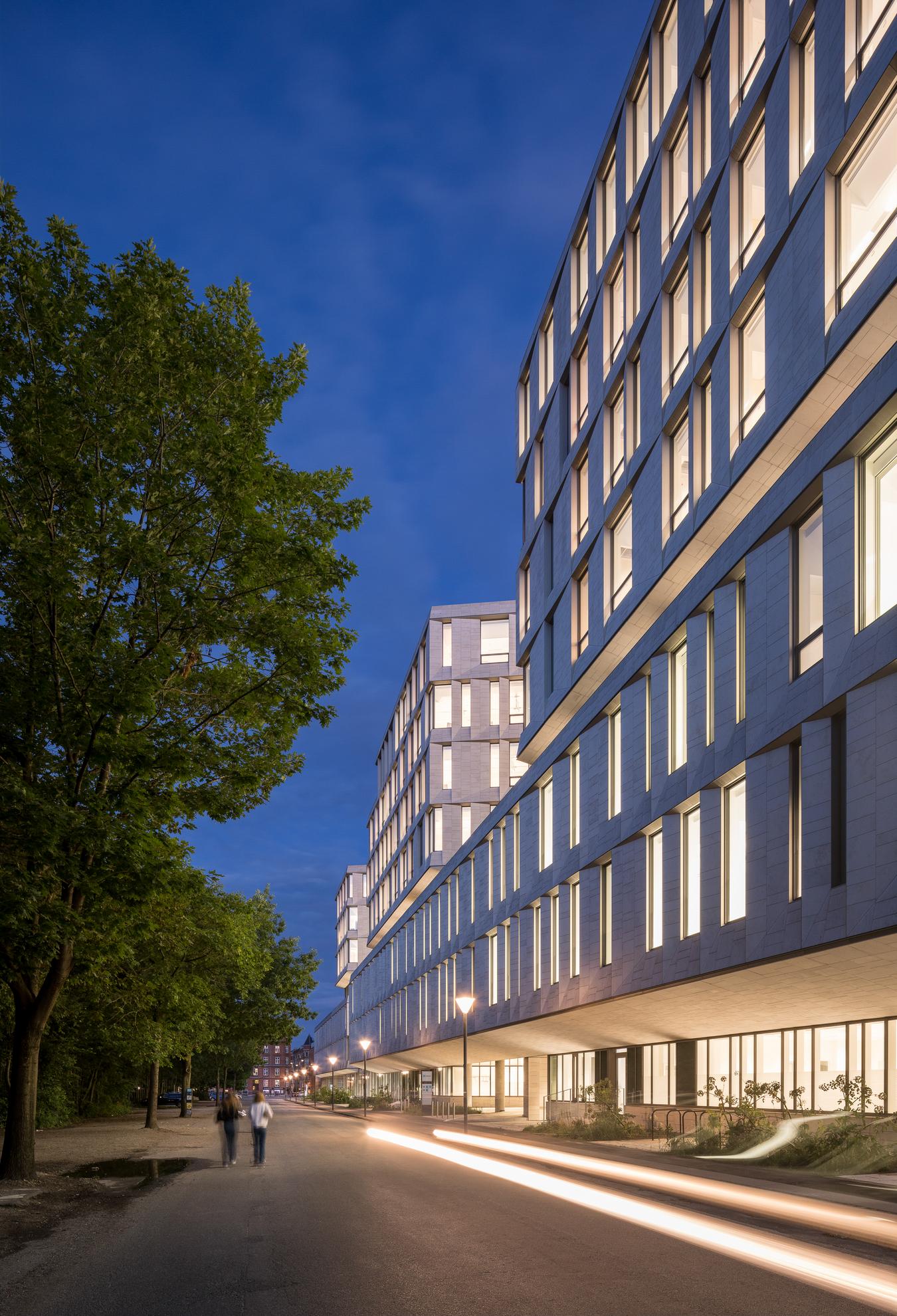 Fotgängare går längs gatan mellan parken och stenbyggnaden. Foto